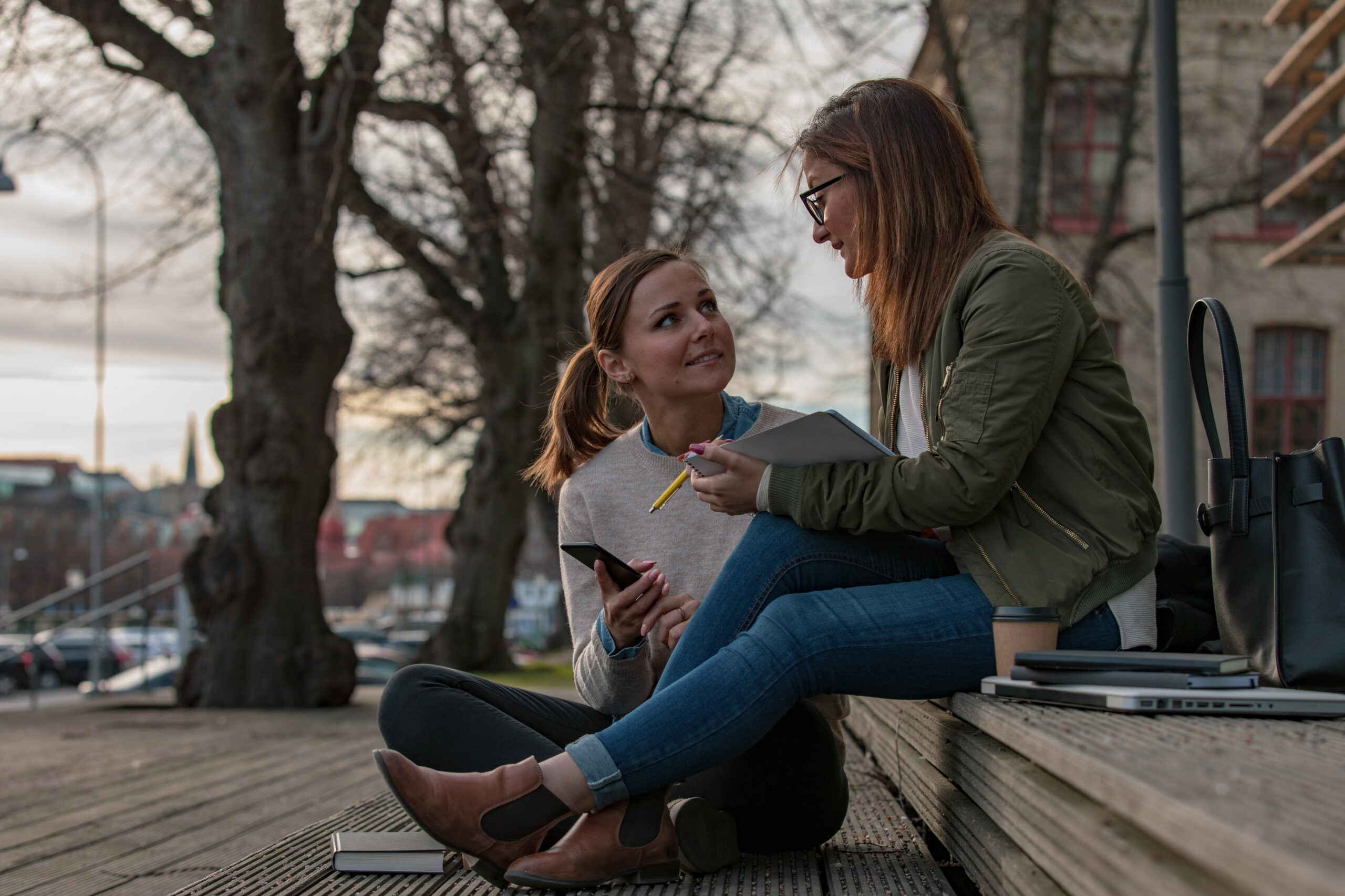 Two women studying in the city Two women are studying outdoors in Gothenburg city. One of them is reading a book and the other one is holding a notebook and a pen.